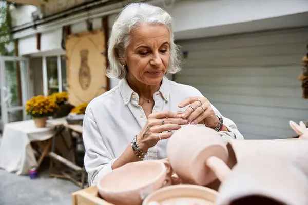 A beautiful mature woman carefully crafts pottery in a vibrant artisan setting surrounded by nature. — Stock Photo