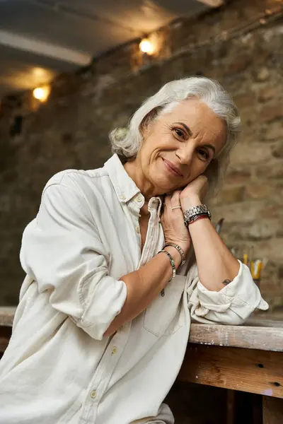 A beautiful mature woman with silver hair radiates warmth while posing in a charming setting. — Stock Photo