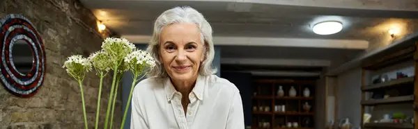 A joyful mature woman stands proudly with fresh flowers, radiating warmth and charm. — Stock Photo