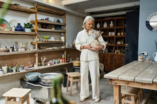 A mature woman enjoys her creative time surrounded by art supplies and handmade pottery. — Stock Photo