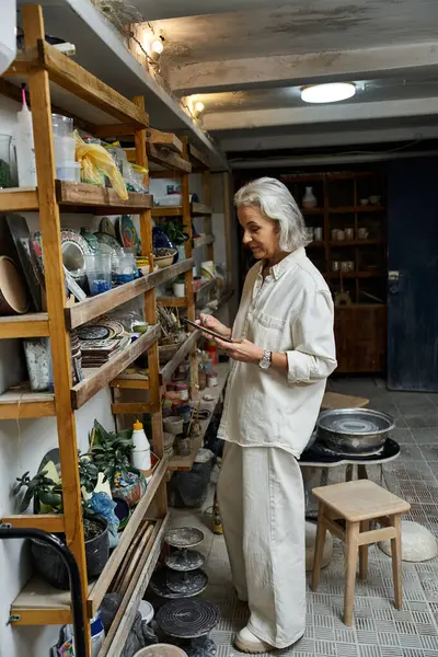 A mature woman immerses herself in her pottery work, examining tools in her art studio. — Stock Photo