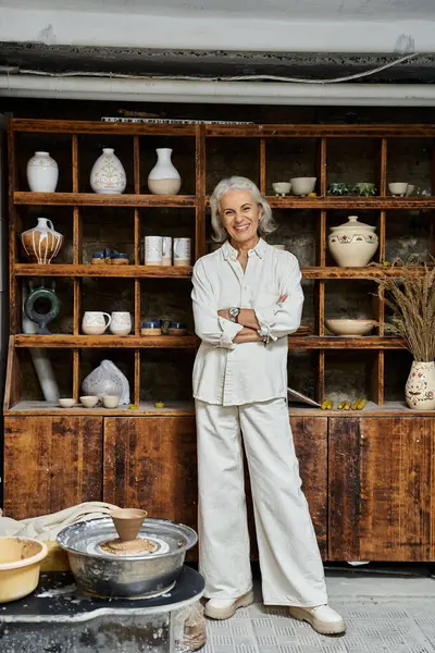 An elegant mature woman smiles in her pottery studio, surrounded by crafted ceramics and art. — Stock Photo