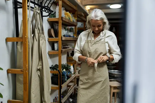A beautiful mature woman dons an apron, focused on her task in a warmly lit workshop. — Stock Photo
