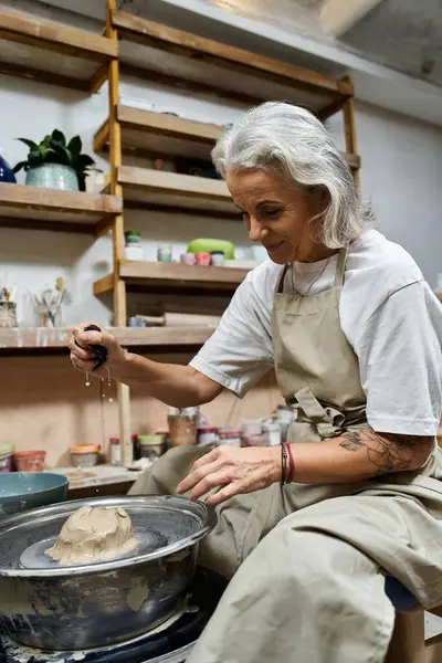 This mature woman skillfully shapes clay on a pottery wheel in her inviting workspace. — Stock Photo