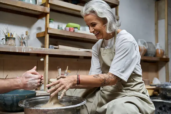 A skilled woman with silver hair expertly molds clay while smiling in her creative workspace. — Stock Photo