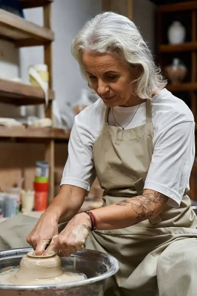 A talented mature woman focuses intently while molding soft clay into a beautiful vessel. — Stock Photo