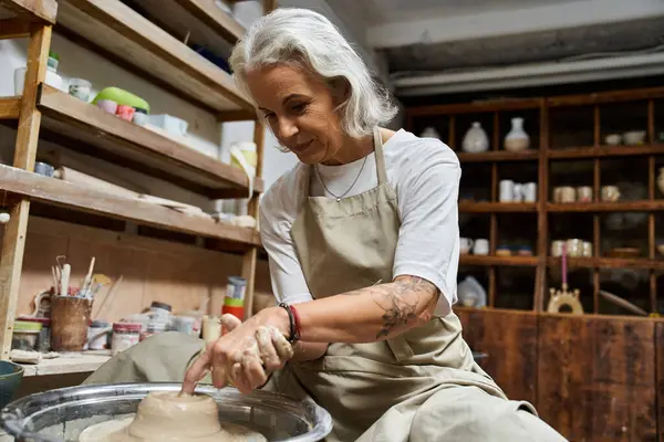 A mature woman skillfully molds clay on a pottery wheel, immersed in creative passion. — Stock Photo