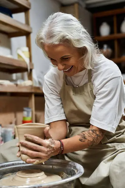 A mature woman immersed in creativity shapes clay, smiling as she crafts her pottery. — Stock Photo