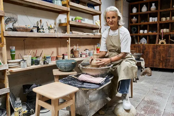 A talented mature woman expertly molds clay in her inviting pottery studio, surrounded by tools. — Stock Photo