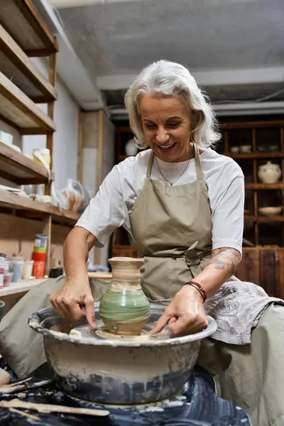 Una mujer talentosa artesanía alegremente una hermosa olla en la rueda de alfareros en su espacio de trabajo artístico. - foto de stock