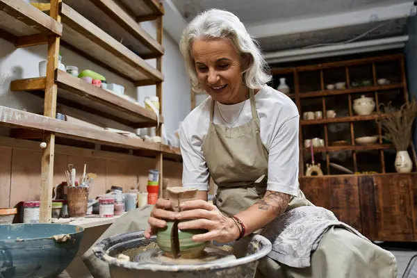 The mature woman shapes clay into a beautiful pot while enjoying her creative process. — Stock Photo