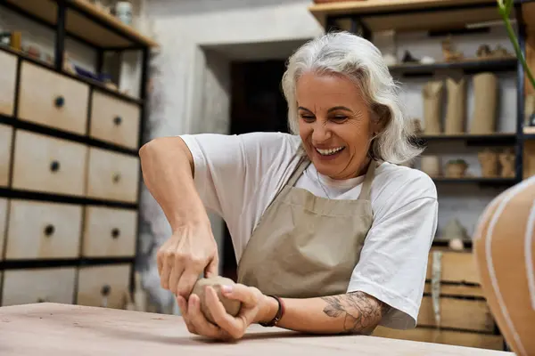 A cheerful mature woman is molding clay with focus and passion in her artistic space — Stock Photo