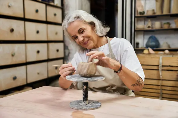 An experienced woman shapes clay on a wheel, showcasing her passion for pottery in a cozy studio. — Stock Photo