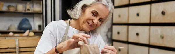 A mature woman passionately sculpts clay, showcasing her artistic talent in her serene workspace. — Stock Photo