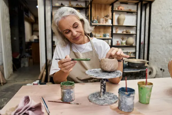 The mature woman skillfully shapes clay while smiling in her inviting artisan studio. — Stock Photo