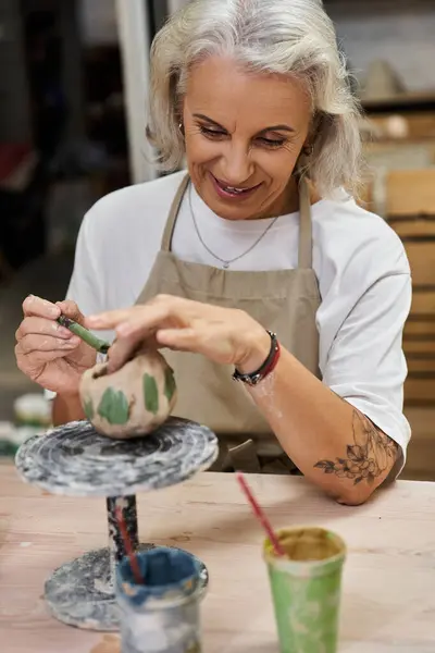 A skilled mature woman carefully shapes her pottery artwork with passion and joy. — Stock Photo
