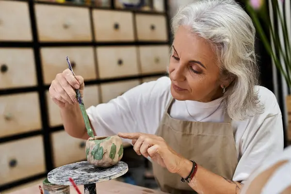 A skilled mature woman focuses on adding details to her pottery project in a vibrant studio. — Stock Photo