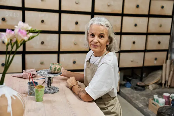 A mature woman engages in pottery crafting, surrounded by artistic materials and storage. — Stock Photo