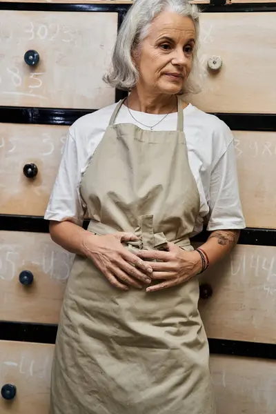 A stylish mature woman exudes confidence while wearing an apron in an artistic workshop setting. — Stock Photo
