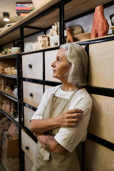 In a pottery workshop, a mature woman reflects on her artistic journey amid crafted pieces. — Stock Photo