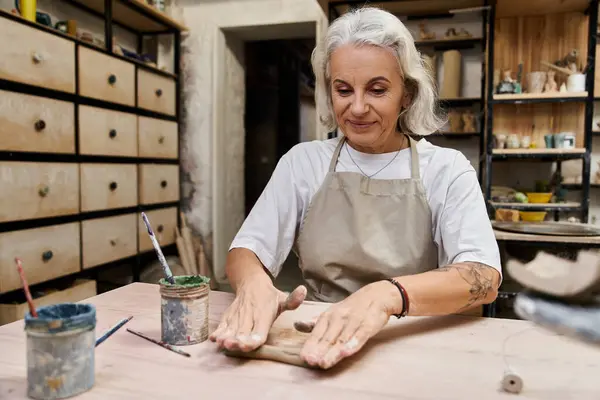 Eine talentierte reife Frau formt an ihrem Arbeitsplatz Ton, umgeben von kreativen Werkzeugen. — Stockfoto