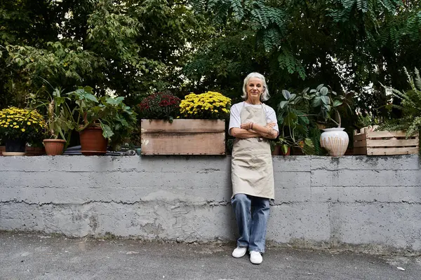 A beautiful mature woman stands proudly among blooming flowers in her lush garden. — Stock Photo