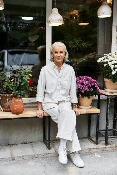 A beautiful mature woman enjoys a peaceful moment surrounded by blooming flowers in a cafe. — Fotografia de Stock