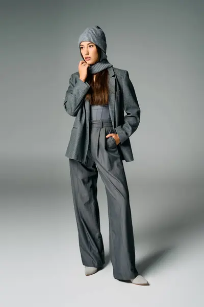 Una giovane donna elegante modella il suo abito grigio chic e accogliente cappello a maglia in uno studio. — Foto stock