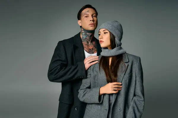 A trendy young couple stands close together, showcasing modern fashion in gray tones. — Stock Photo