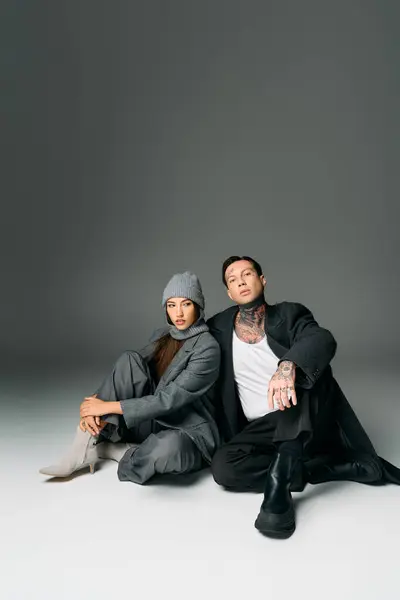 A young attractive duo sits closely on the floor, showcasing trendy urban fashion with confidence. — Stock Photo