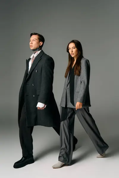 A young couple dressed in elegant grey outfits struts confidently in a contemporary studio. — Stock Photo