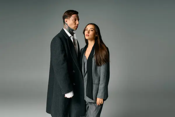 A young attractive couple poses intimately while showcasing elegant gray attire in soft lighting. — Stock Photo