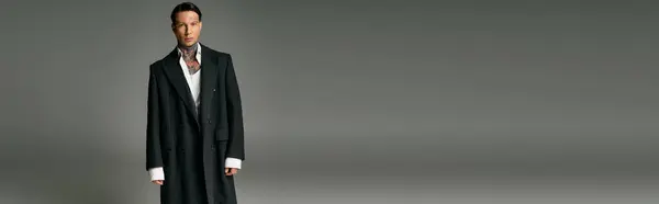 The young man stands tall, exuding charisma in a chic long coat fitting the modern aesthetic. — Stock Photo
