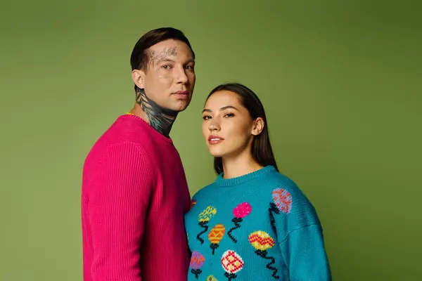 A trendy young couple models colorful sweaters in a creative setting with a green background. — Stock Photo