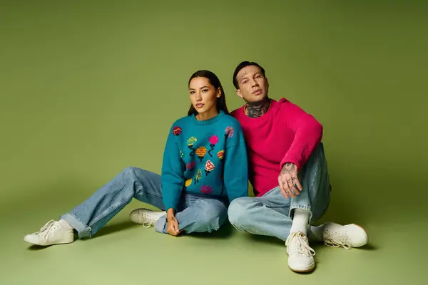 A young and attractive couple sits casually on a green backdrop, expressing unique fashion styles. — Stock Photo