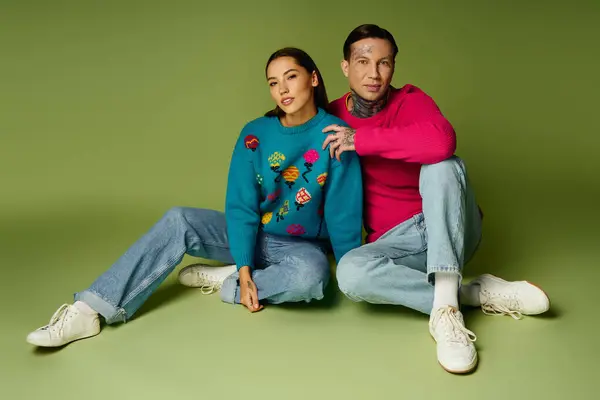 Stylish duo poses together on the floor, highlighting their unique sweaters in playful colors. — Stock Photo