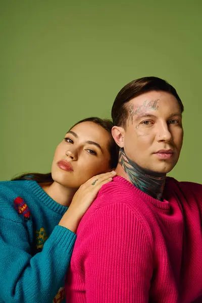Una joven pareja hace alarde de su estilo con suéteres de colores y tatuajes llamativos. - foto de stock