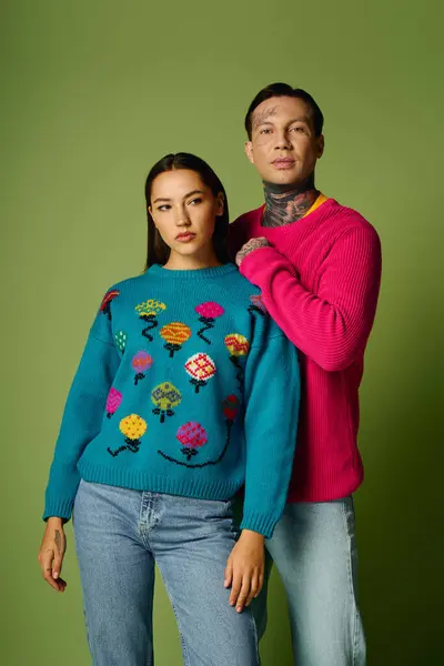 A stylish young couple stands confidently, showcasing vibrant sweaters with a playful design. — Stock Photo