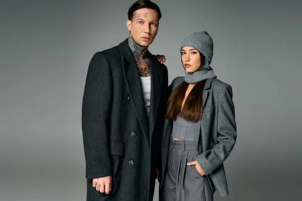 A stylish young couple poses confidently in warm winter attire against a muted background. — Stock Photo