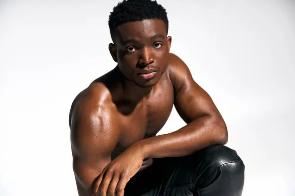 A young, attractive African American man poses topless with a relaxed yet confident expression. His strong physique is emphasized in the well lit studio setting, highlighting his charisma. — Stock Photo