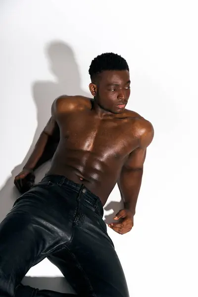 A young African American man showcases his athletic physique in a stylish pose, leaning against a clean white background. His confident expression and body language exude charisma and elegance. — Stock Photo