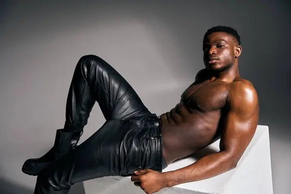 A young, athletic African American man showcases his toned physique while lounging on a minimalist structure. His relaxed pose highlights confidence and strength. — Stock Photo