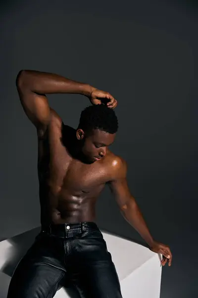 A young handsome African American man poses confidently, displaying his toned physique and sense of style. The artistic setting emphasizes his striking features and charm. — Stock Photo