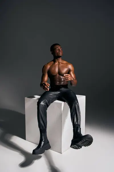 In a sleek studio, a young and handsome African American man poses topless on a white pedestal, exuding confidence and charisma. — Stock Photo