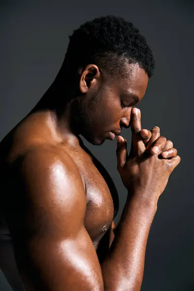 A young handsome African American man strikes a contemplative pose, showcasing his toned physique. The studio lighting highlights his features and adds depth to the artistic ambiance. — Stock Photo