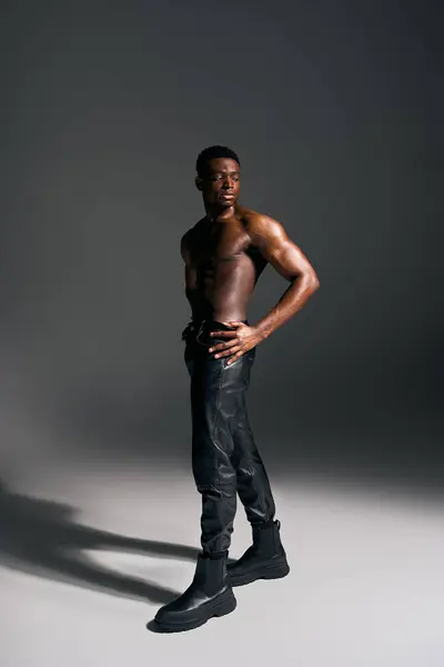 A young handsome African American man stands confidently, showcasing his toned physique in a creative studio with dramatic lighting. The artistic atmosphere enhances his striking presence. — Stock Photo