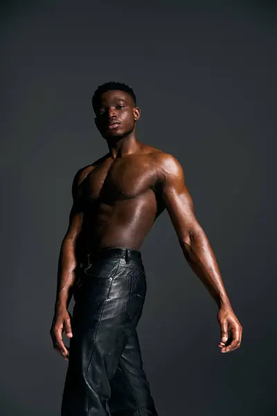 A young, handsome African American man poses confidently without a shirt. His toned physique is highlighted against a dark background, creating a bold and captivating presence. — Stock Photo