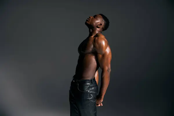 A young handsome African American man stands confidently with a powerful pose, showcasing his physique in a studio. — Stock Photo