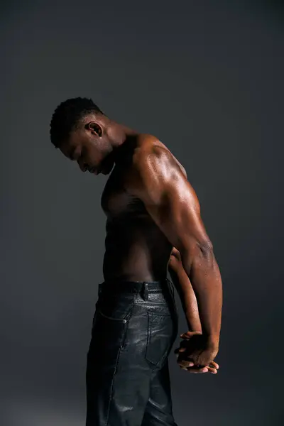 Ein junger und gut aussehender afrikanisch-amerikanischer Mann steht selbstbewusst oben ohne in einem modernen Studio. Seine athletische Statur wird durch eine dramatische Beleuchtung unterstrichen, die eine kraftvolle und dynamische Atmosphäre schafft. — Stockfoto