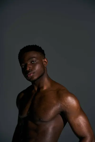 A young handsome african american man showcases his toned physique, striking a pose against a dark background. His confident gaze and subtle shine enhance the artistic ambiance of the moment. — Stock Photo